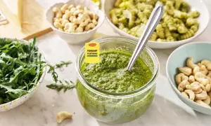 Słoik pełen aromatycznego pesto z rukoli, obok miseczki z orzechami nerkowca i świeżą rukolą. Idealne do makaronu!
