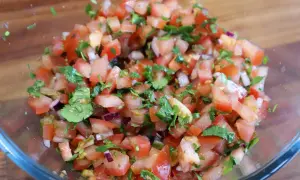 Świeża, kolorowa salsa z pomidorów, cebuli i kolendry w szklanej misce. Idealna do nachos lub jako dodatek do dań.