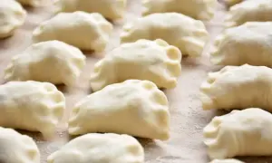 Gotowe do gotowania ciasto na pierogi, ułożone rzędami na blacie.