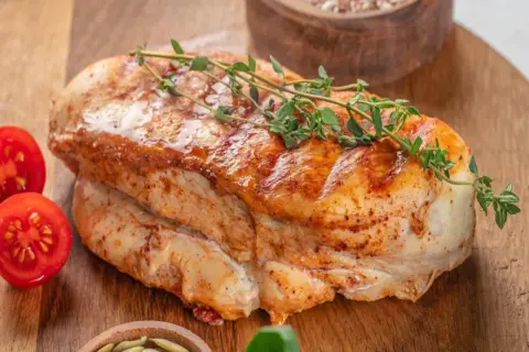 Soczysty, pieczony filet z indyka z gałązką tymianku i pomidorkami koktajlowymi na drewnianej desce.
