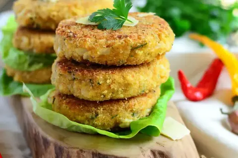 Złociste kotlety z kalafiora, chrupiące i aromatyczne, ułożone na sałacie. Obok czerwone i żółte papryczki chili.