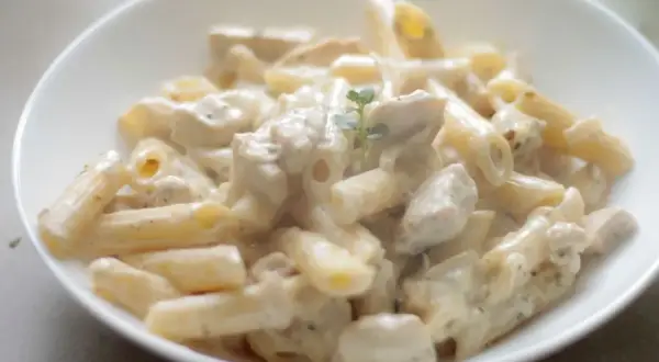 Penne z kurczakiem w kremowym sosie, udekorowane gałązką ziół. Pyszne danie, które zachwyci każdego smakosza makaronu z kurczakiem.