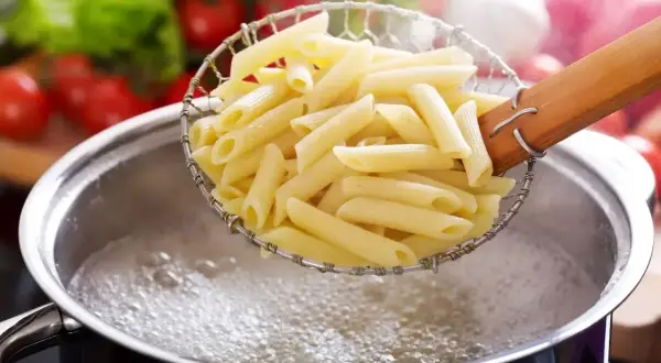 Penne w cedzaku nad garnkiem z wrzącą wodą. Idealny sposób, jak ugotować makaron, by był al dente.