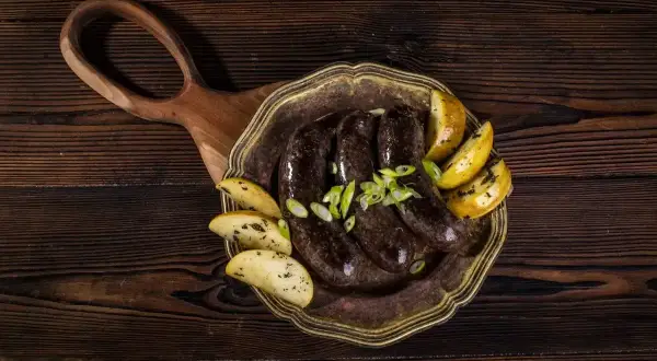 Pyszna kaszanka z piekarnika, podana z pieczonymi ziemniakami i szczypiorkiem, na drewnianej desce.