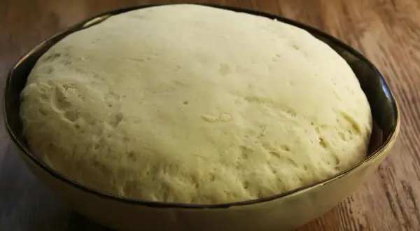 Puszyste ciasto na pizzę wyrosło w misce, gotowe do dalszej obróbki.
