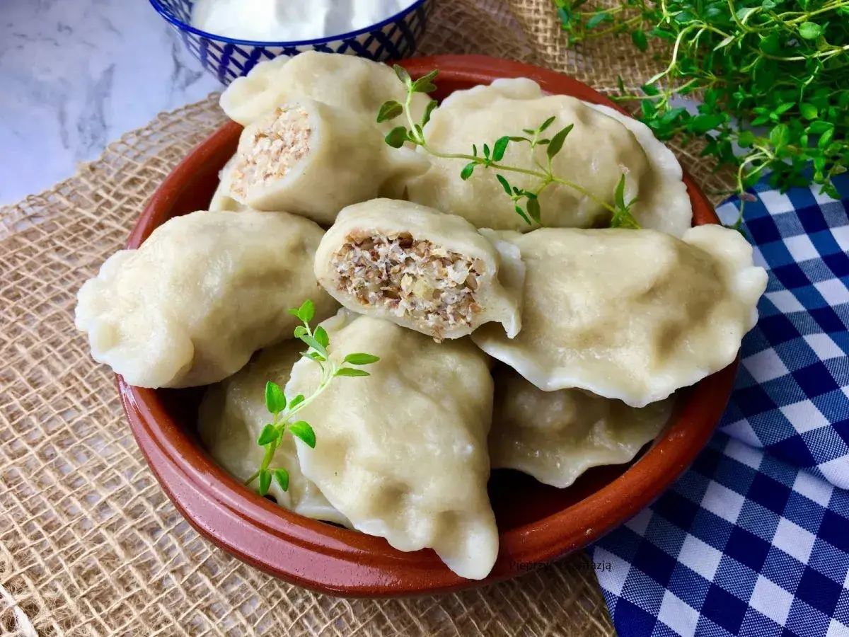 Pyszne pierogi z kaszą gryczaną i twarogiem, udekorowane gałązkami ziół, kuszą swoim domowym wyglądem.
