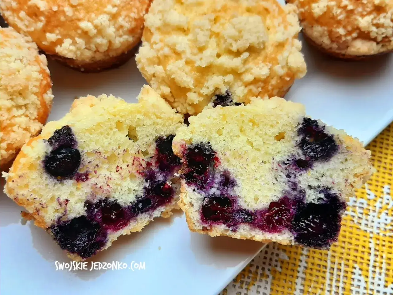 Puszyste muffinki z bor&oacute;wkami, jedna przekrojona, ukazująca soczyste owoce. Kruszonka na wierzchu dodaje uroku.