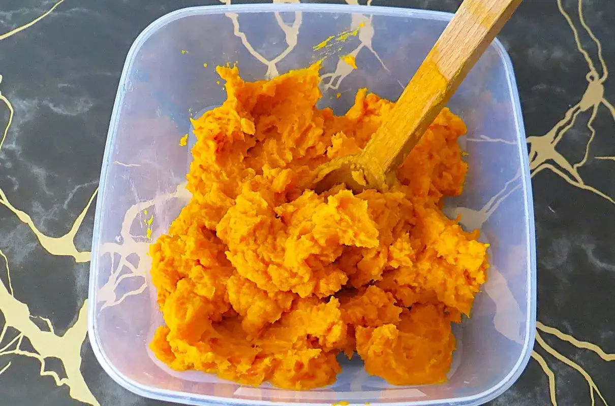Jasne, pomarańczowe puree z dyni hokkaido w plastikowym pojemniku, gotowe do dalszego wykorzystania.