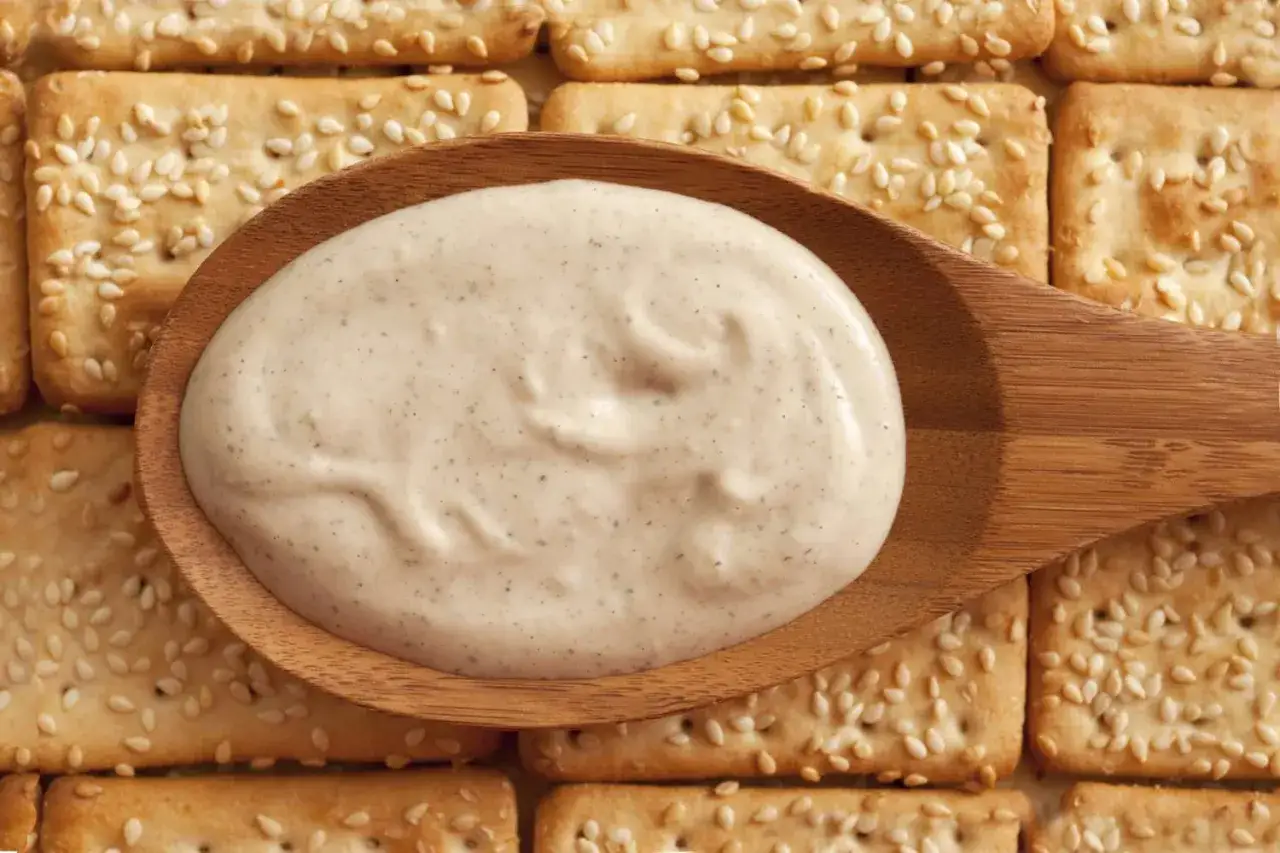 Kremowy sos na drewnianej łyżce, idealny do krakersów z sezamem. Czy to tahini? Co to jest?