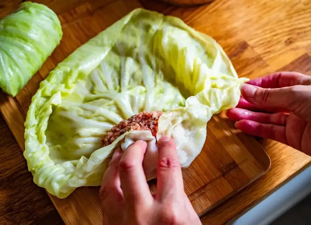Ręce zwijają gołąbki z farszem mięsnym w liście kapusty. To początek pysznego przepisu na gołąbki na 1kg mięsa.