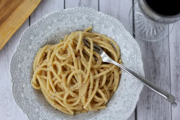 Porcja pysznego cacio e pepe z widelcem w talerzu, gotowa do zjedzenia.