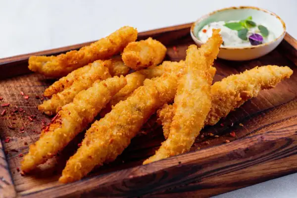 Chrupiące filet z kurczaka w cieście, podane na drewnianej desce z dipem. Idealne na przekąskę.