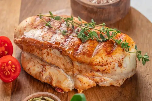 Soczysty, pieczony filet z indyka z gałązką tymianku i pomidorkami koktajlowymi na drewnianej desce.