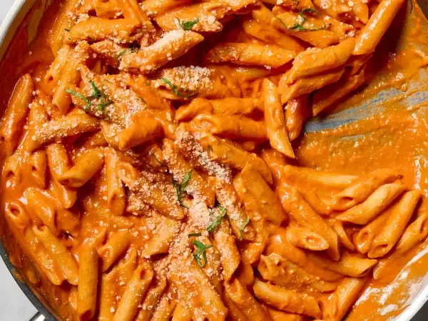 Penne alla vodka w kremowym, pomarańczowym sosie, posypane parmezanem i świeżą bazylią.