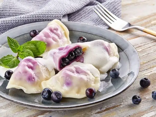 Pyszne pierogi z jagodami, polane śmietaną, ozdobione miętą i świeżymi owocami. Idealne na deser!