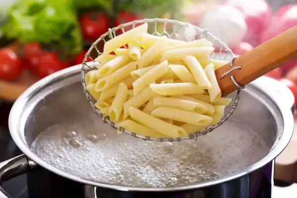 Penne w cedzaku nad garnkiem z wrzącą wodą. Idealny sposób, jak ugotować makaron, by był al dente.