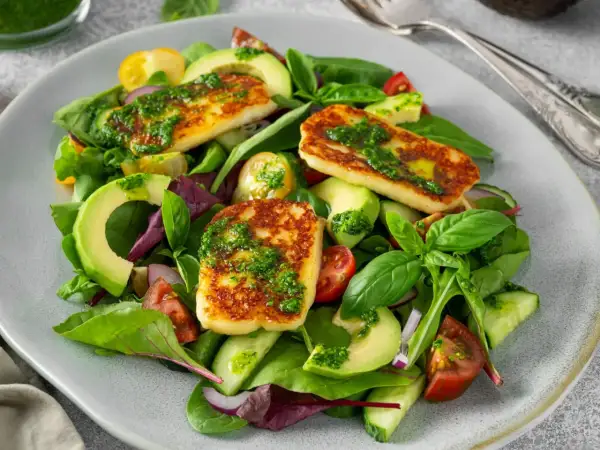 Pyszna sałatka z halloumi, awokado, pomidorkami i ogórkiem, polana zielonym sosem.